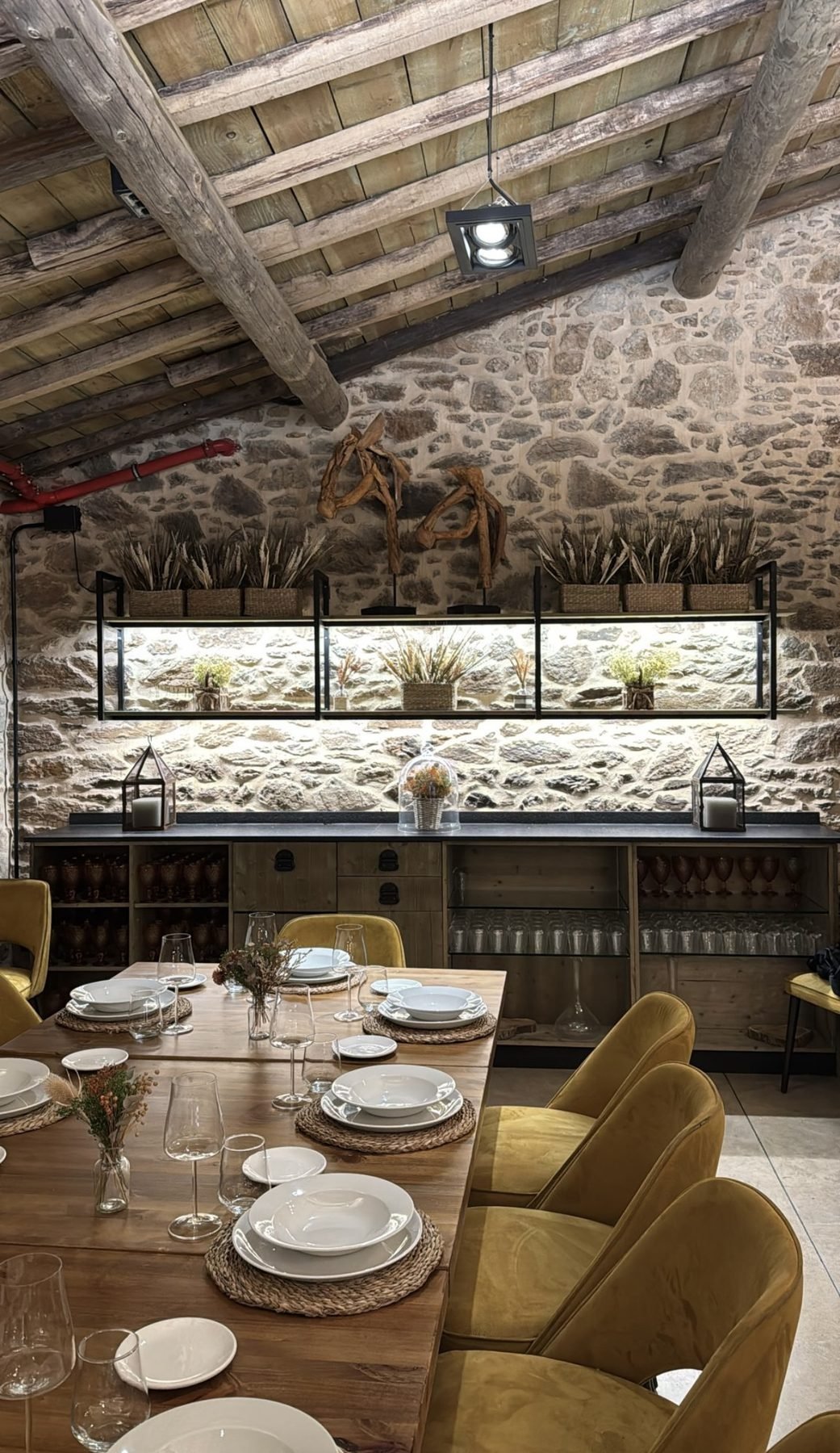 Comedor con mesa vestida, muro de granito y vigas de madera