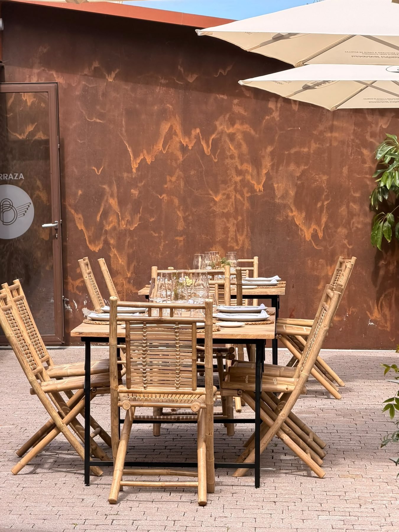Mesas de madera en la terraza, frente al muro de acero corten