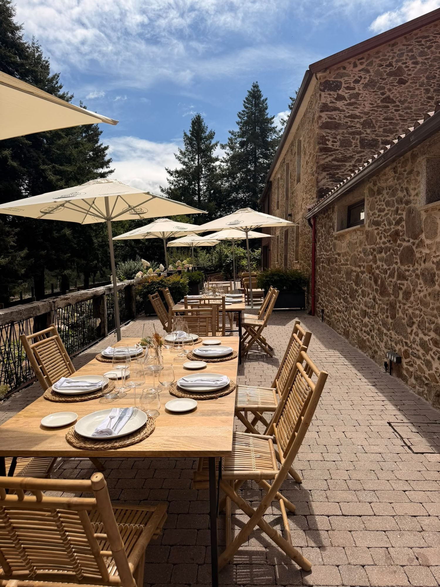 Terraza con mesas vestidas y parasoles junto al muro de piedra